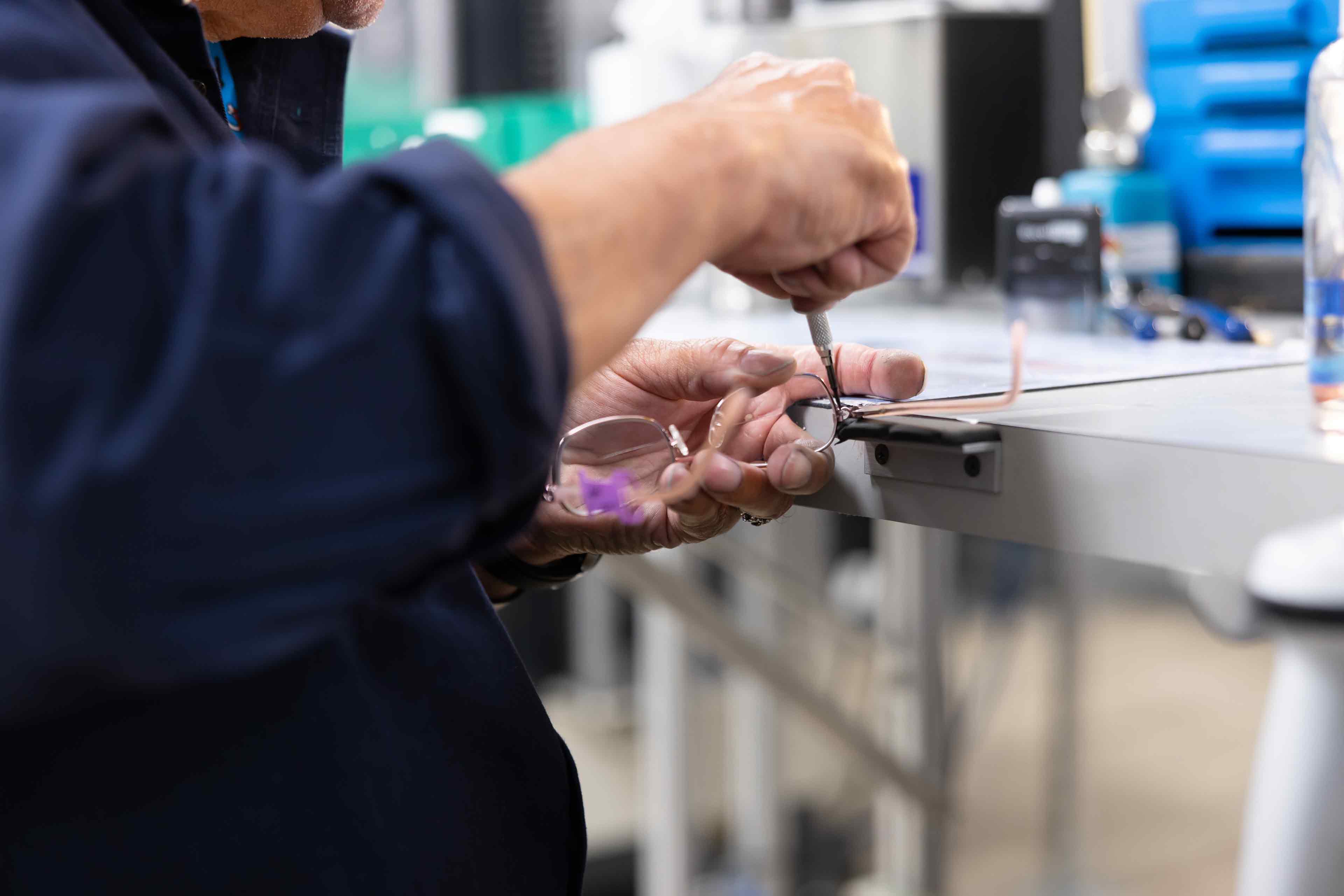 Person working on a small eyeglass component with tools in a workshop setting
