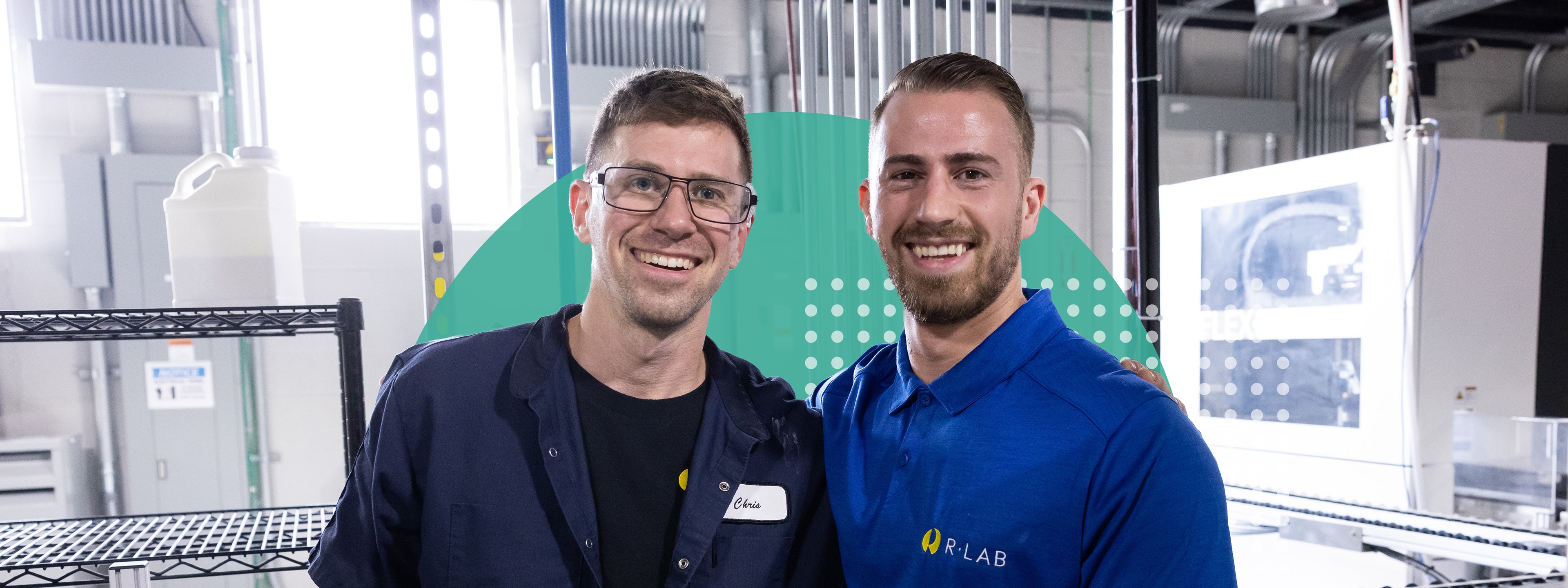 Two men standing in a factory setting with a green circular logo in the background