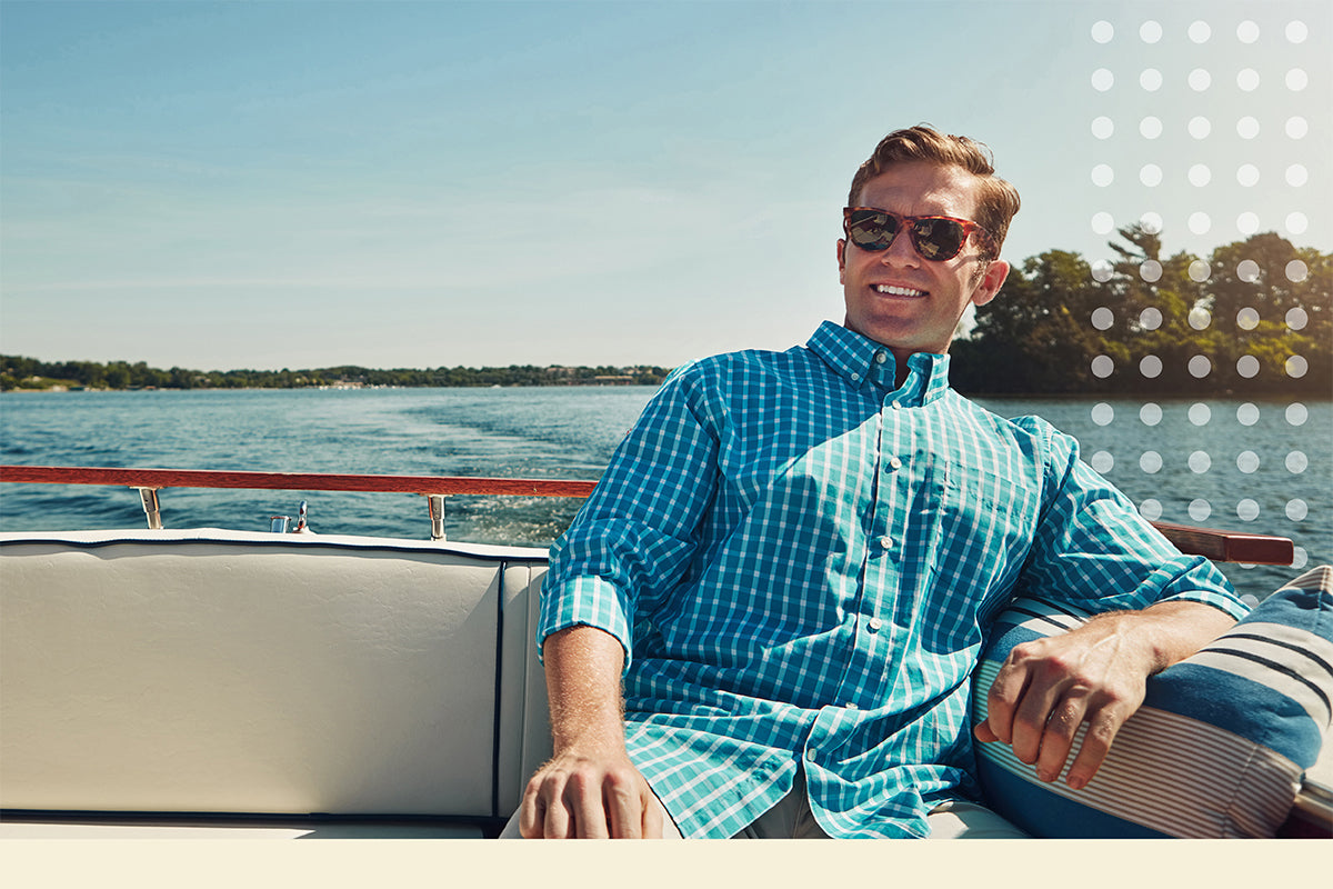 Man in a blue checkered shirt sitting on a boat with water and trees in the background
