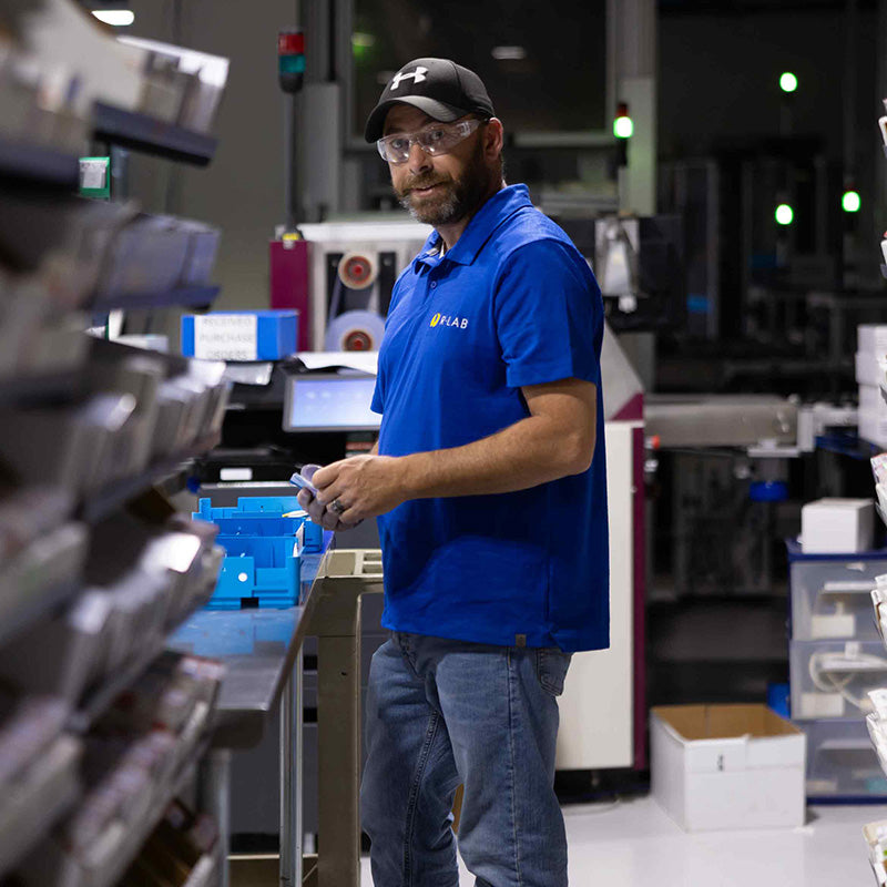 Man in a blue shirt with a Rlab logo in the lab holding a lens.