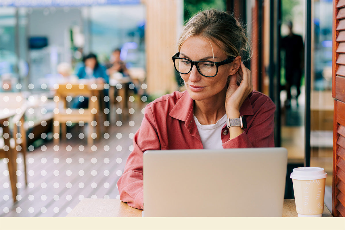 Woman using a laptop in a cafe setting with eyeglasses on.