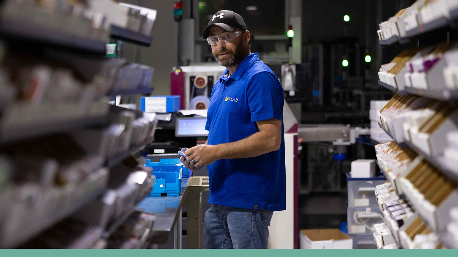 Person in a blue shirt and cap working in a Rlab setting with shelves and equipment.