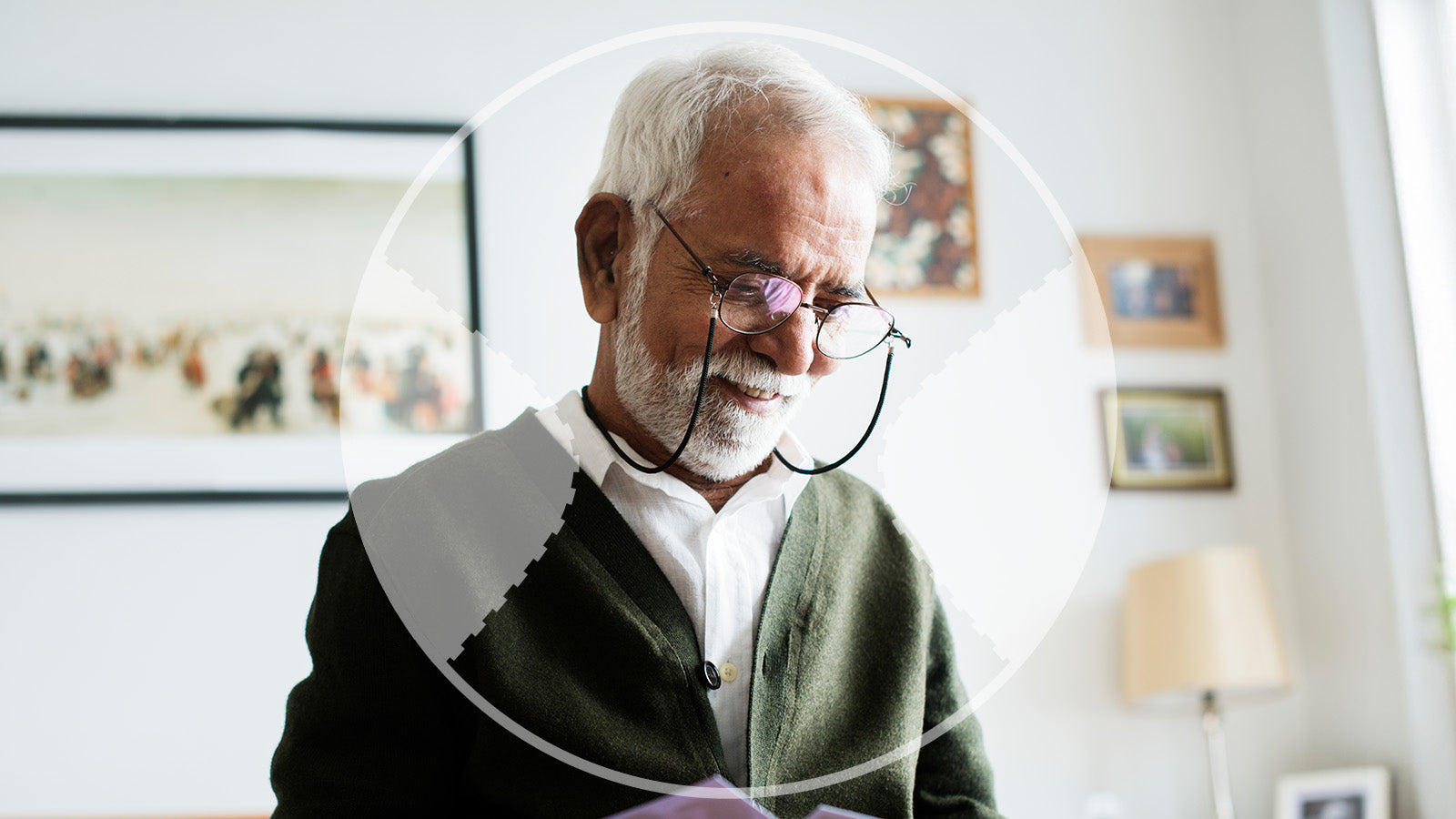 Senior man wearing glasses and a green sweater in a room with framed pictures on the wall.