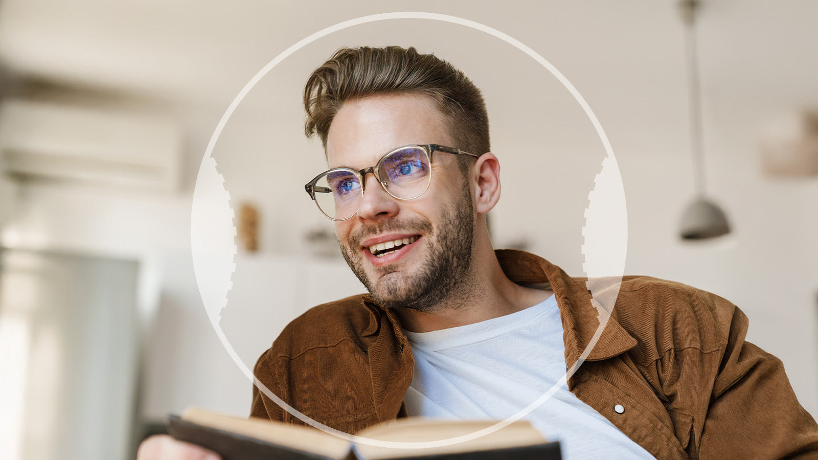 Man wearing glasses and a brown jacket holding a book indoors.