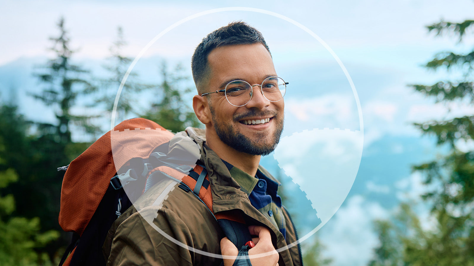Man with a backpack smiling outdoors with trees and mountains in the background